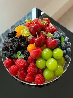 a glass bowl filled with lots of different types of fruit on top of a table