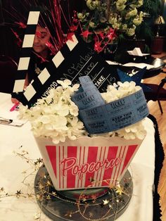 a popcorn bucket filled with white flowers and movie claps on top of a table