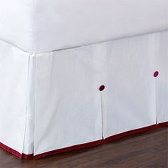 a white bed with red trim and buttons on the bottom side, along with a wooden floor