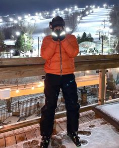 a man standing on top of a snow covered slope next to a ski lift at night