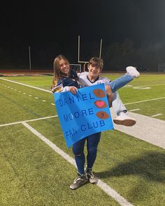 two people holding a sign that says danielle moore fan club on the sidelines at night