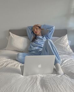 a woman sitting on a bed with her laptop in front of her head and hands behind her head