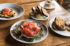 three plates of food on a table with bread, salad and other foods in the background