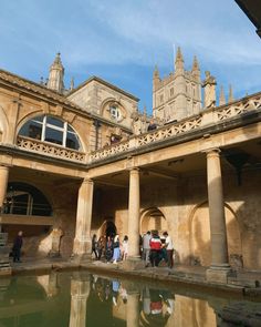 some people are standing around in front of a building with columns and arches on the roof