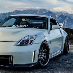 the front end of a white sports car parked on top of a rocky mountain range