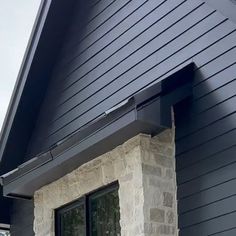 the side of a house with black siding and stone window sill on it's corner