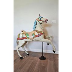 an old fashioned carousel horse is standing on a wooden floor in front of a white wall