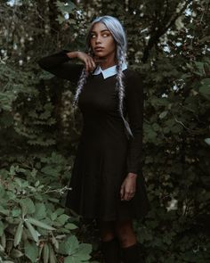 a woman with grey hair wearing a black dress and boots standing in front of trees