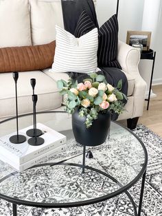 a coffee table with flowers on it in front of a couch and two candlesticks