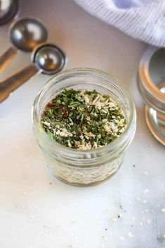 a glass jar filled with herbs on top of a counter next to measuring spoons