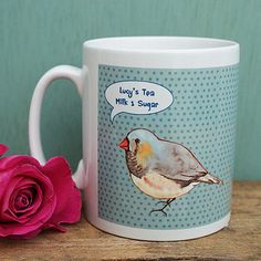 a coffee mug with a bird on it next to a pink rose and a blue background