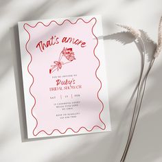 a pink and red wedding card on top of a white table with dried flowers next to it