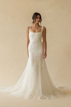 a woman in a white wedding dress standing against a beige background with her back to the camera