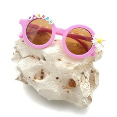 a pair of pink sunglasses sitting on top of a piece of white rock next to a flower