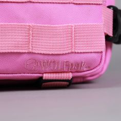 a pink bag with black handles and straps on the bottom half is sitting on a gray surface