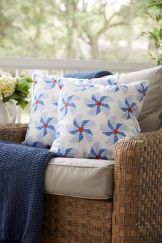 a wicker chair with blue and red pillows on it, next to a basket filled with flowers