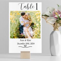 a table number card with an image of a couple on it and flowers in the vase