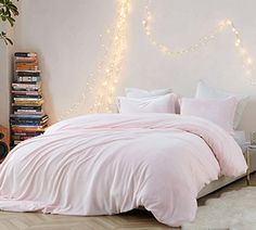 there is a bed with pink sheets and pillows on the floor next to bookshelves