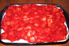 a pan filled with strawberries and sauce on top of a wooden table next to a plate