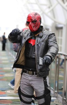 a man wearing a red mask and leather jacket standing in front of a metal railing