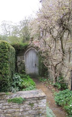 an old stone building with a wooden door surrounded by greenery and trees in the background