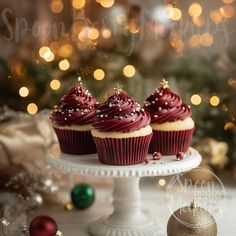 three red velvet cupcakes on a white cake plate with christmas decorations in the background