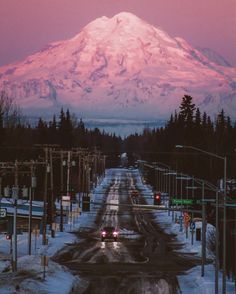 a snow covered mountain in the distance with traffic lights on it's sides and cars driving down the road