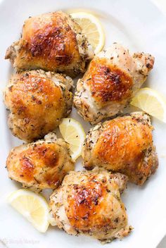 lemon chicken thighs on a white plate with sliced lemons and parmesan cheese