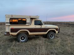 an old truck with a camper on the back parked in a field at sunset