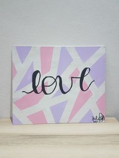 a painting with the word love painted on it sitting on a wooden shelf in front of a white wall