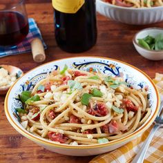 pasta with tomatoes and basil in a bowl on a wooden table next to two bottles of wine