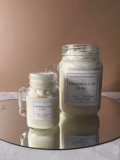 two jars filled with white candles sitting on top of a glass table next to each other