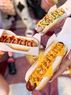 two people holding hot dogs with toppings on them