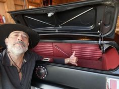 a man wearing a cowboy hat sitting in front of a car trunk with his thumb up