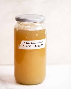 a glass jar filled with chicken sauce on top of a white counter next to a silver lid