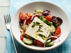 a white bowl filled with vegetables and tofu on top of a blue table cloth