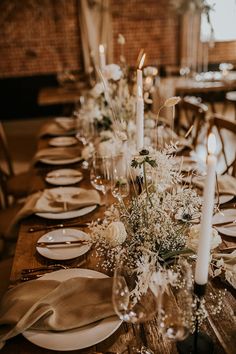 the table is set with white plates and silverware, candles, and greenery