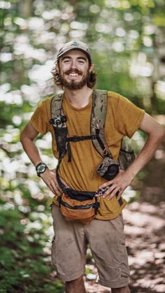 a man standing in the woods with his hands on his hips and smiling at the camera