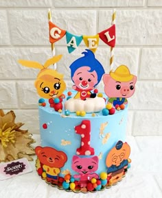 a birthday cake decorated with cartoon characters and candles for a child's first birthday