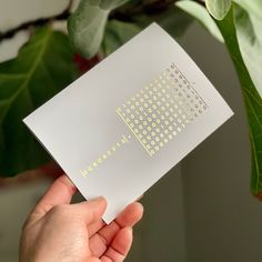 a person holding up a piece of paper with dots on it in front of a plant