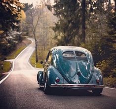 an old blue car is driving down the road