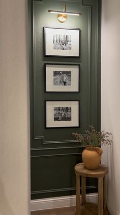 a green wall with pictures on it and a small wooden table in front of it