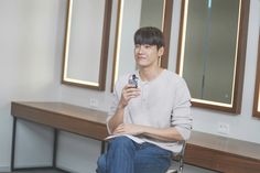 a young man sitting on a bench holding a cell phone in his right hand and smiling at the camera