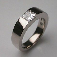 a white gold ring with a princess cut diamond set in the center, on a grey background