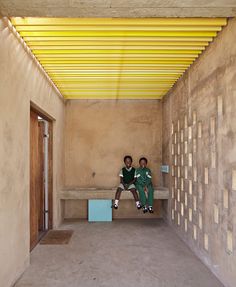 two people sitting on a bench in a room with yellow beams above them and walls