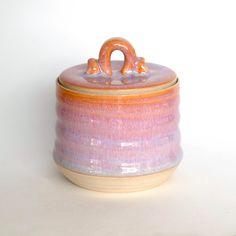 a pink and orange ceramic container with a wooden handle on white table top next to wall