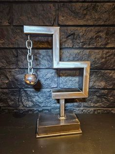 a metal sculpture on top of a table next to a wall with a ball and chain hanging from it