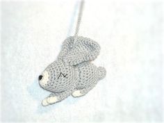 a crocheted gray teddy bear hanging from a chain on a white background with the letter m