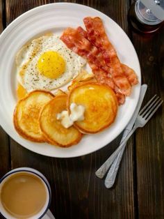 a plate with eggs, bacon and pancakes on it next to a cup of coffee