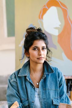 a woman sitting in front of a painting holding a piece of paper and looking at the camera